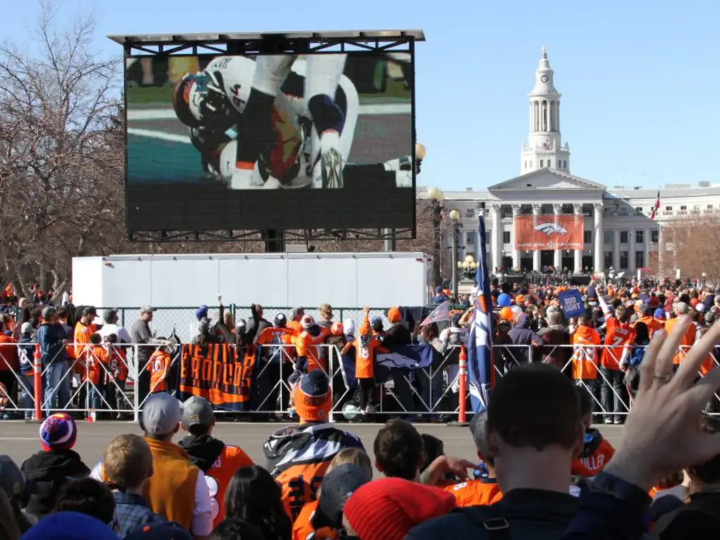 Mobile LED screen trailer, displaying live football coverage for a large outdoor watch party with fans gathered for a game-day event.