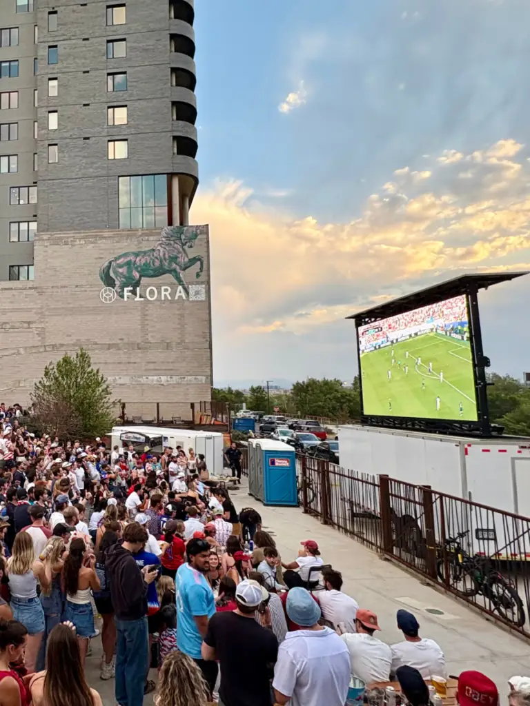 Crowd watching a live soccer match on a mobile led screen during an outdoor watch party in an urban event venue.