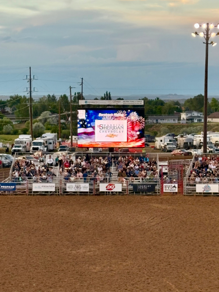 Mobile LED screen displaying sponsor and event content during a packed rodeo event with grandstand spectators and arena viewing.