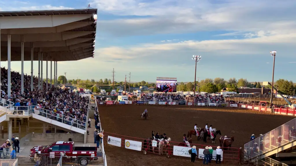 Mobile LED screen displaying live rodeo action to a packed grandstand during an outdoor evening rodeo event.