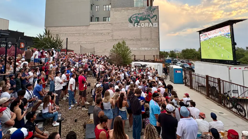 Crowd watching a live soccer match on a mobile led screen during an outdoor watch party in an urban event venue.
