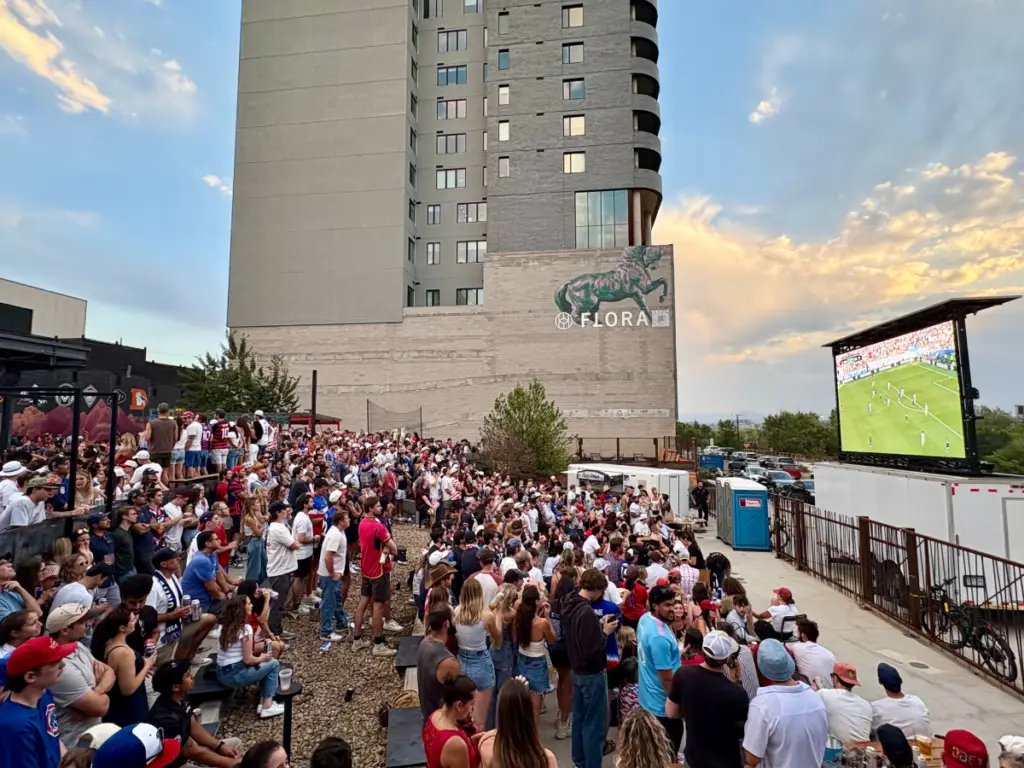 Crowd watching a live soccer match on a mobile led screen during an outdoor watch party in an urban event venue.