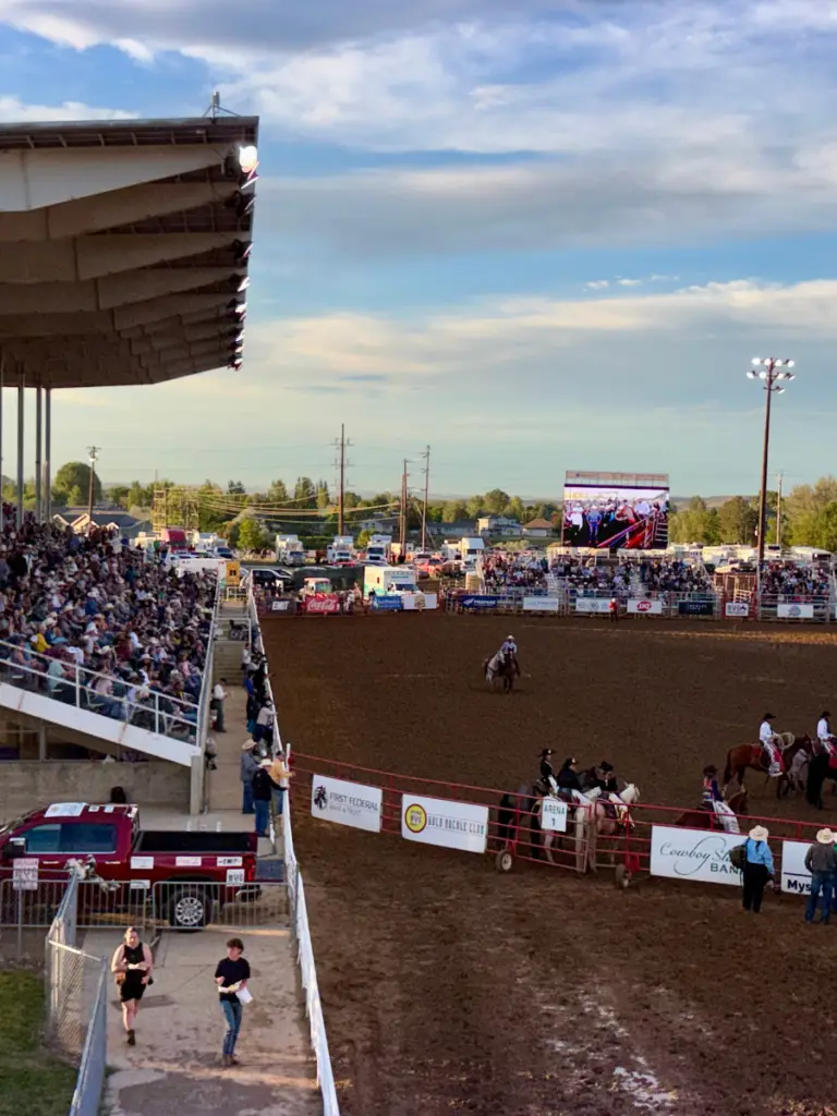 Mobile LED screen displaying live rodeo action to a packed grandstand during an outdoor evening rodeo event.