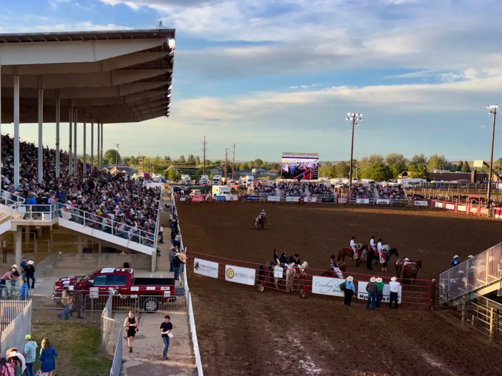 Mobile LED screen displaying live rodeo action to a packed grandstand during an outdoor evening rodeo event.