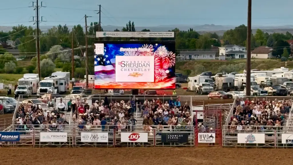Mobile LED screen displaying sponsor and event content during a packed rodeo event with grandstand spectators and arena viewing.