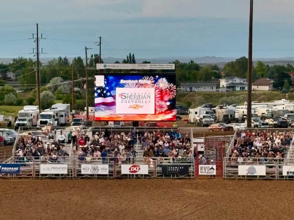 Mobile LED screen displaying sponsor and event content during a packed rodeo event with grandstand spectators and arena viewing.